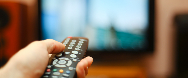 A TV remote control pointed at a blurred television set