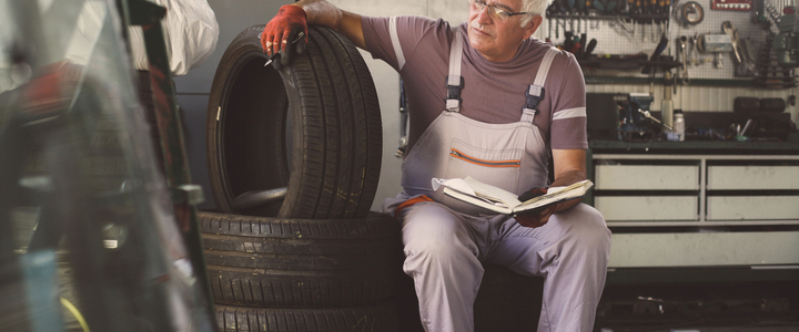 An elderly mechanic sits on a stack of tyres while managing his accounts