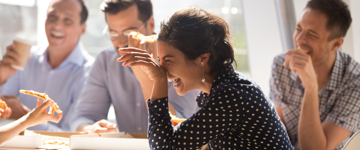 Colleagues laughing and eating pizza over a business lunch