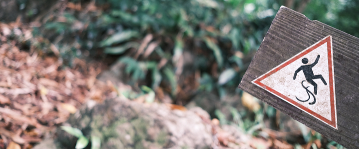 A “slip hazard” warning sign on a leafy and rocky downhill path