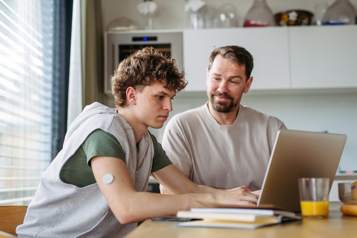 Father helping son with work on his laptop.